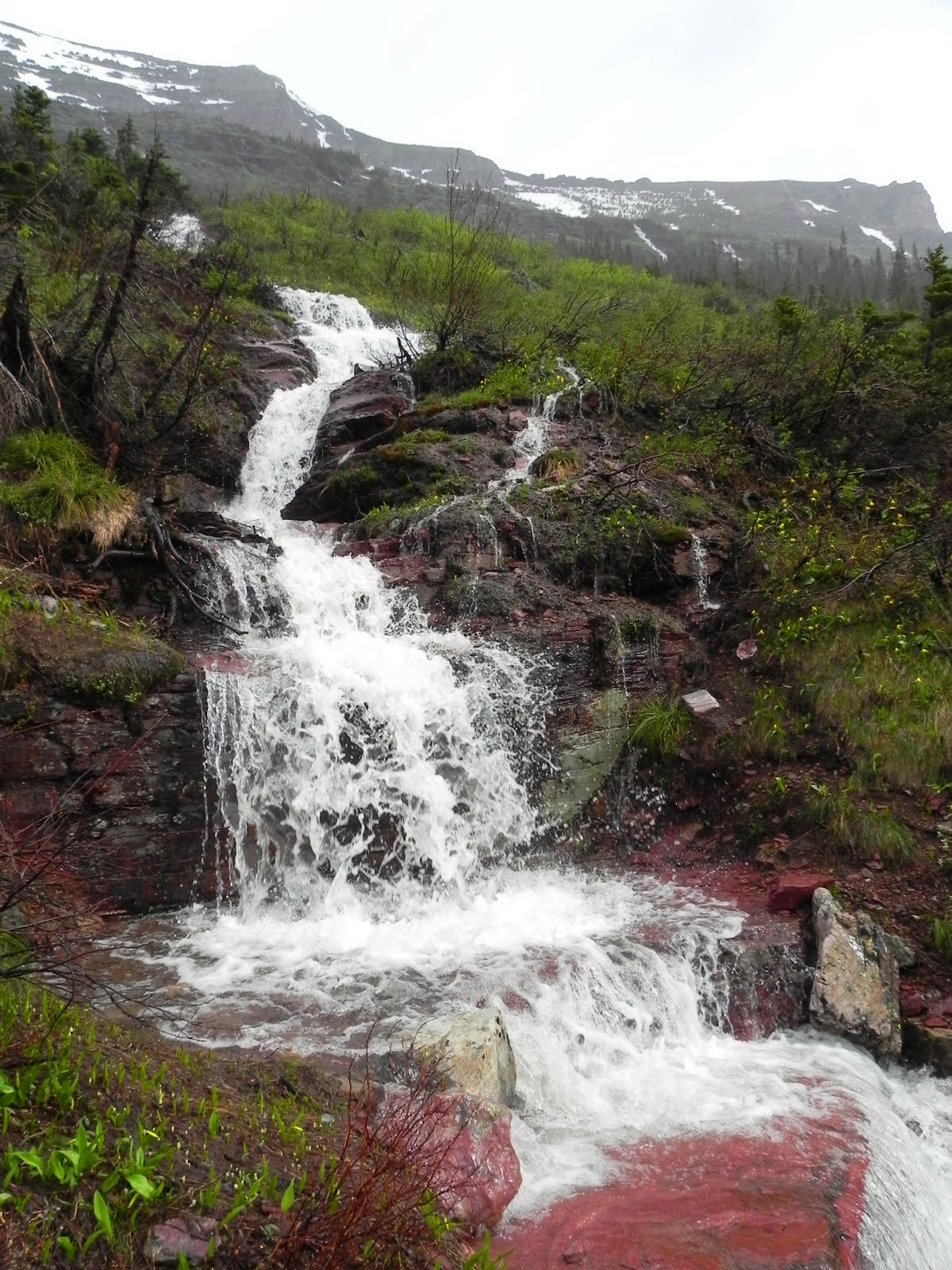Grinnell Glacier Trail 旁流过红色岩石的季节性雪融瀑布